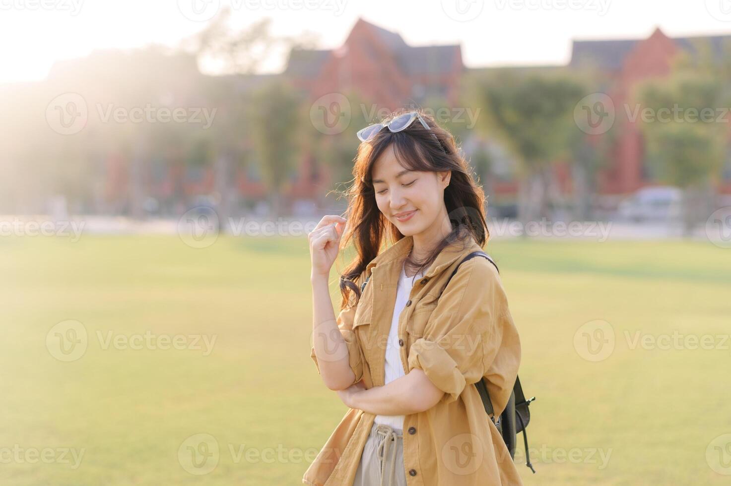 Southeast asian woman enjoys peaceful moment outdoors with gentle smile, embracing travel concept in sunny park setting with casual clothing and natural light photo