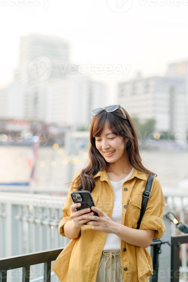 Southeast asian woman enjoys travel concept using smartphone outdoors in city with happy smile wearing casual clothes and sunglasses on her head photo
