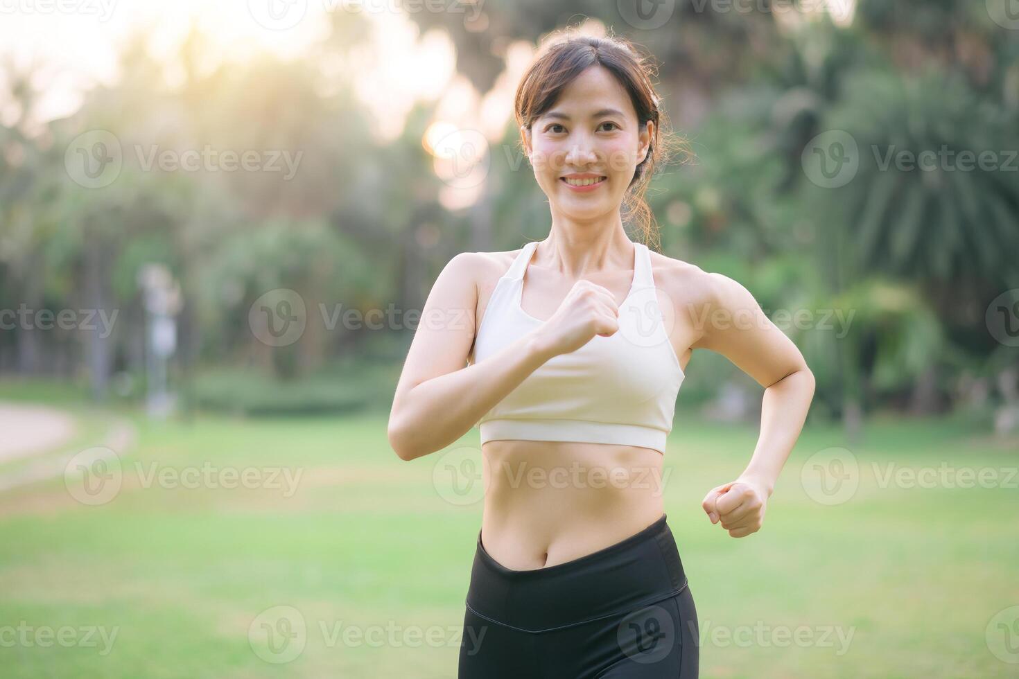 Southeast asian woman enjoying wellness and healthy lifestyle concept through outdoor exercise jogging in park with cheerful expression and natural sunlight photo
