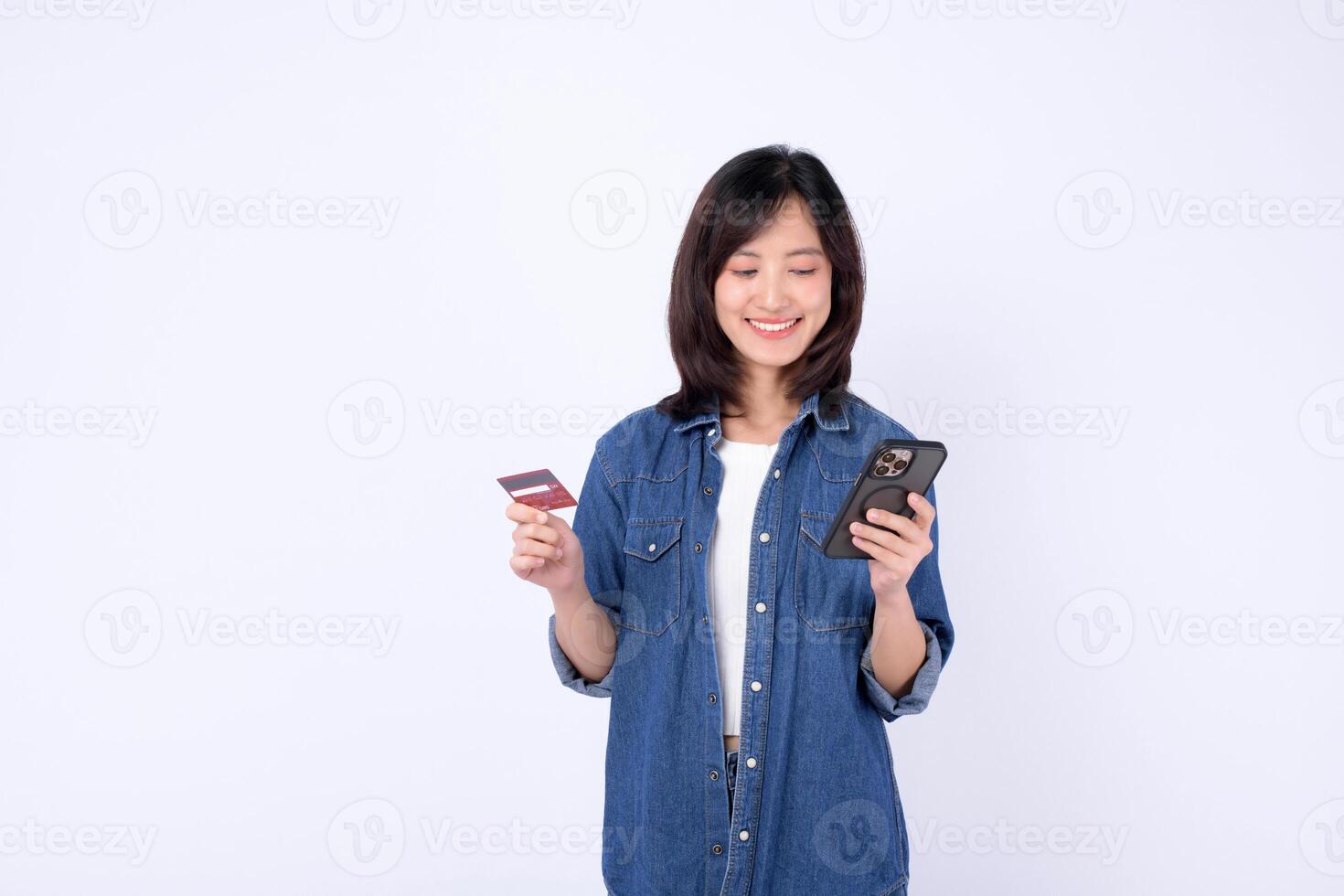 Southeast asian woman smiling while using internet for online shopping holding credit card and smartphone against white background photo
