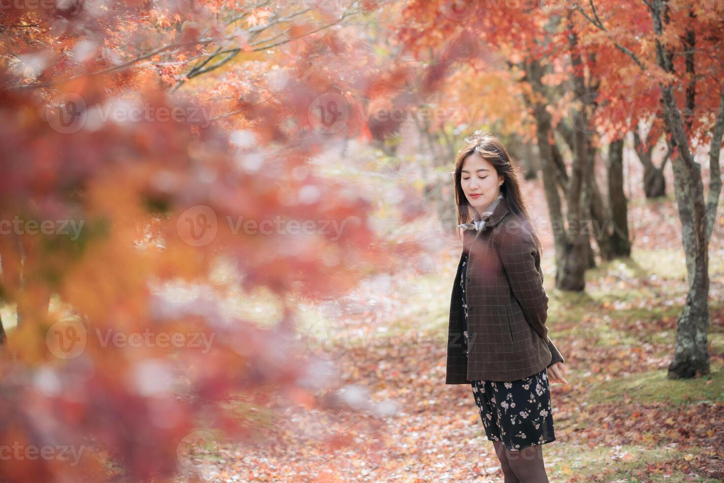 Southeast Asian woman enjoys travel in autumn forest with colorful leaves and peaceful atmosphere, standing among vibrant orange and red trees in nature photo