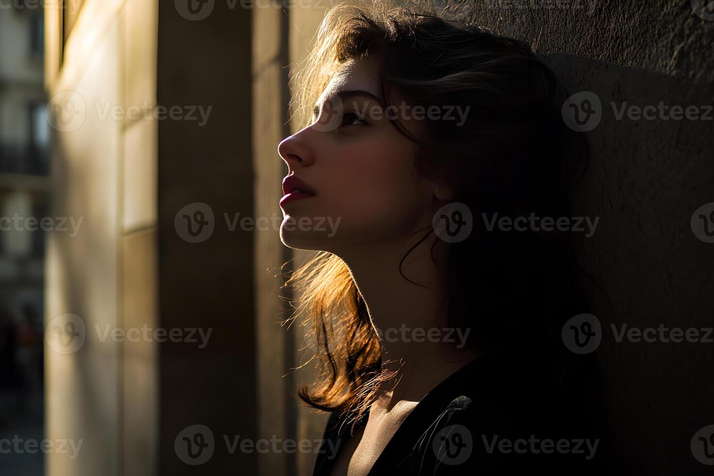 Dreamy portrait of a girl gazing upwards bathed in a golden sunlight on a shadowed wall in outdoor setting. photo