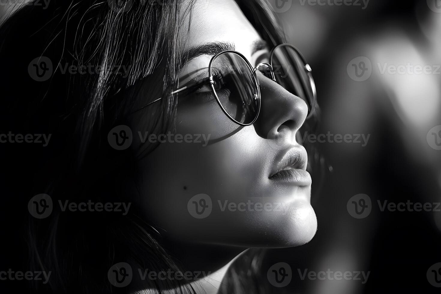 Black and white close-up of a woman wearing round sunglasses in dramatic lighting High contrast. photo