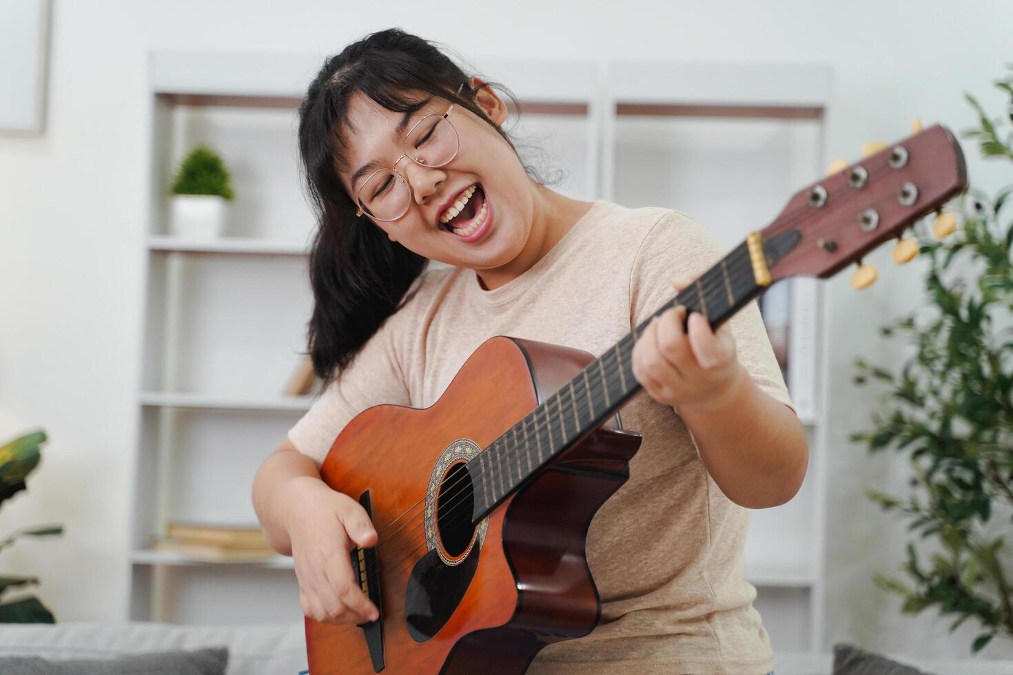 Asian woman play acoustic guitar and singing on the sofa in living room at home photo