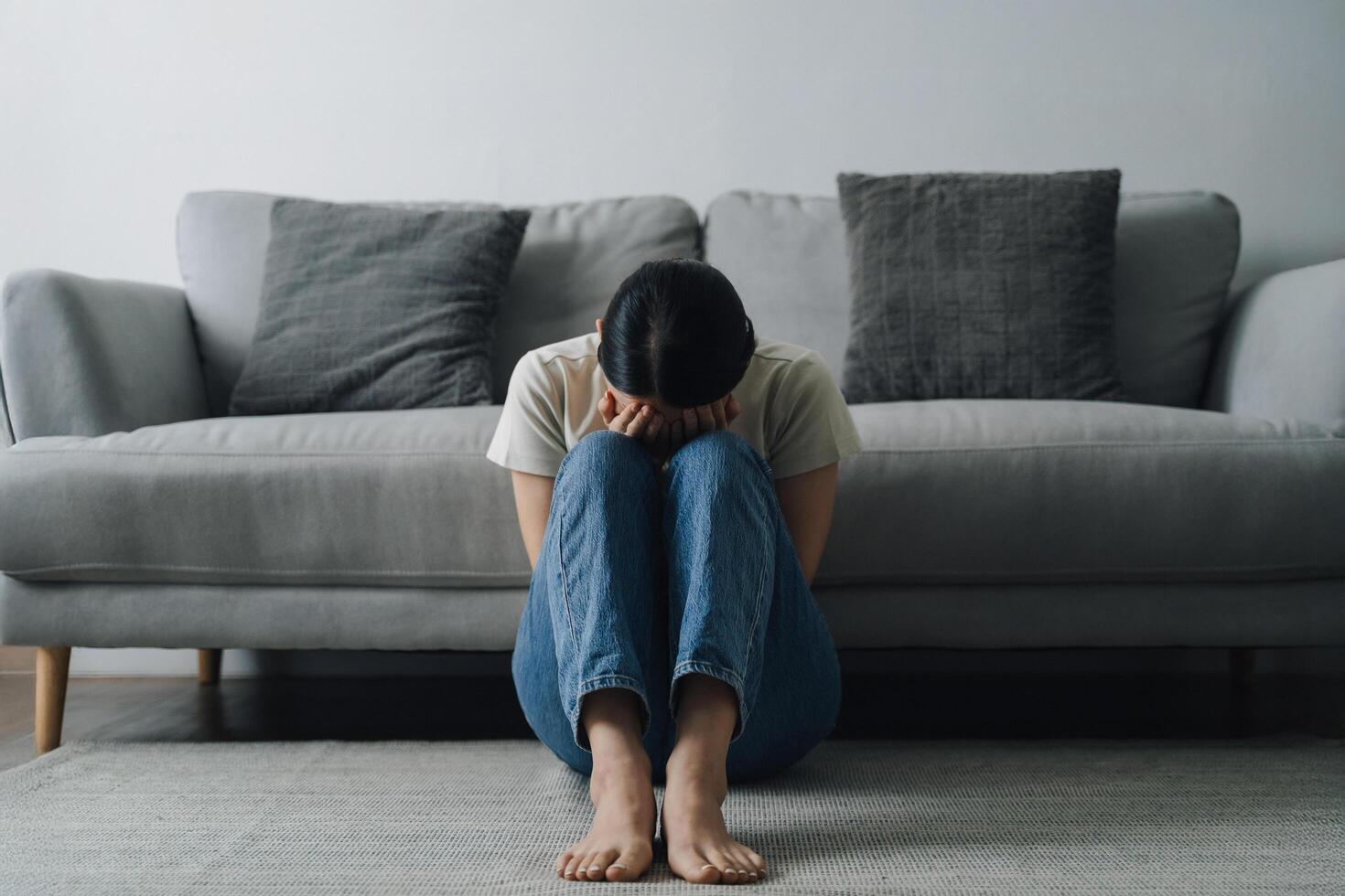 Woman is sitting on the floor in a living room. She is crying and she is in a state of distress photo