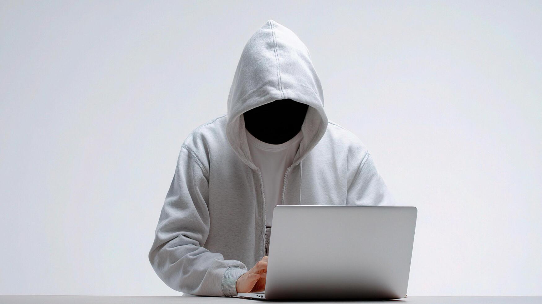 A person in a hoodie sitting at a desk with a laptop photo