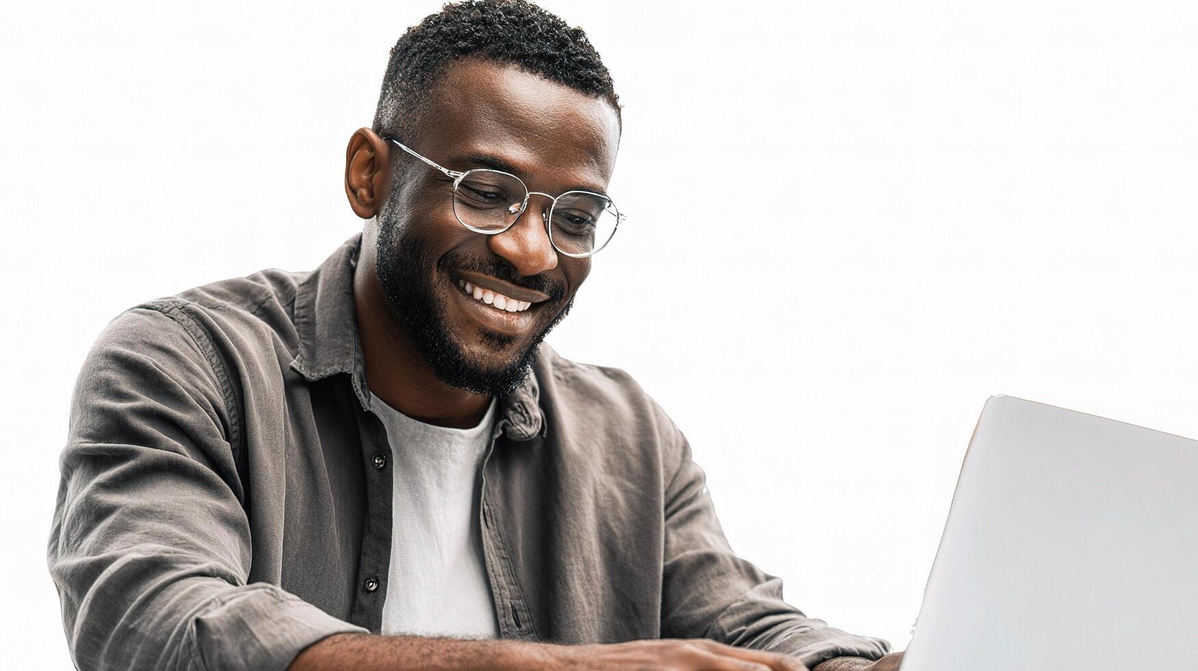 A smiling black man with glasses is using a laptop photo