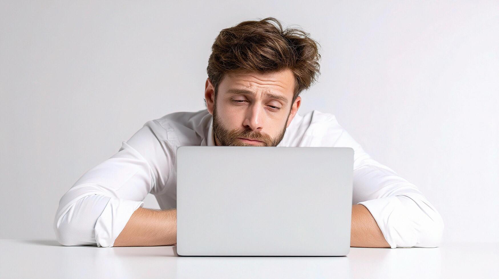A man is sitting at a table with his head on his laptop photo