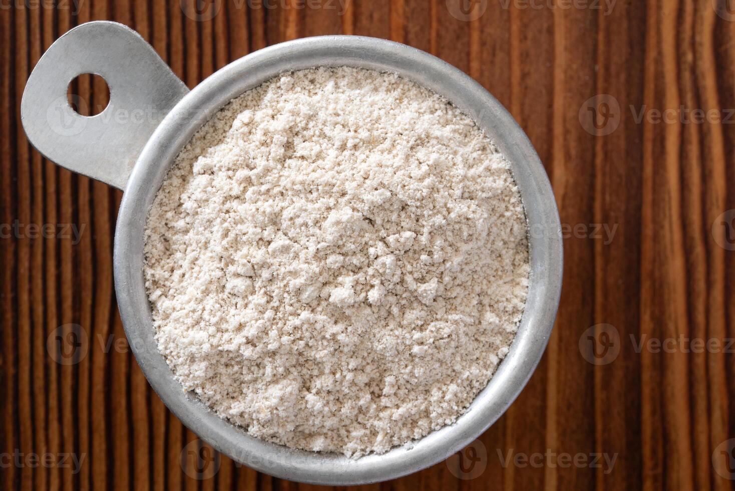 Uncooked Oat Flour in a Vintage Measuring Cup on Wood Background photo