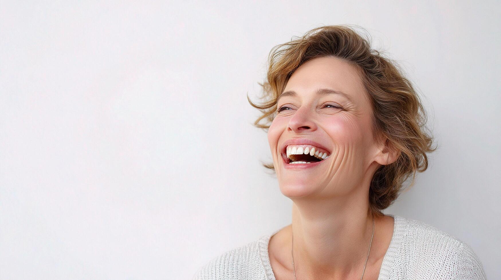 A woman laughing and smiling in front of a white wall photo