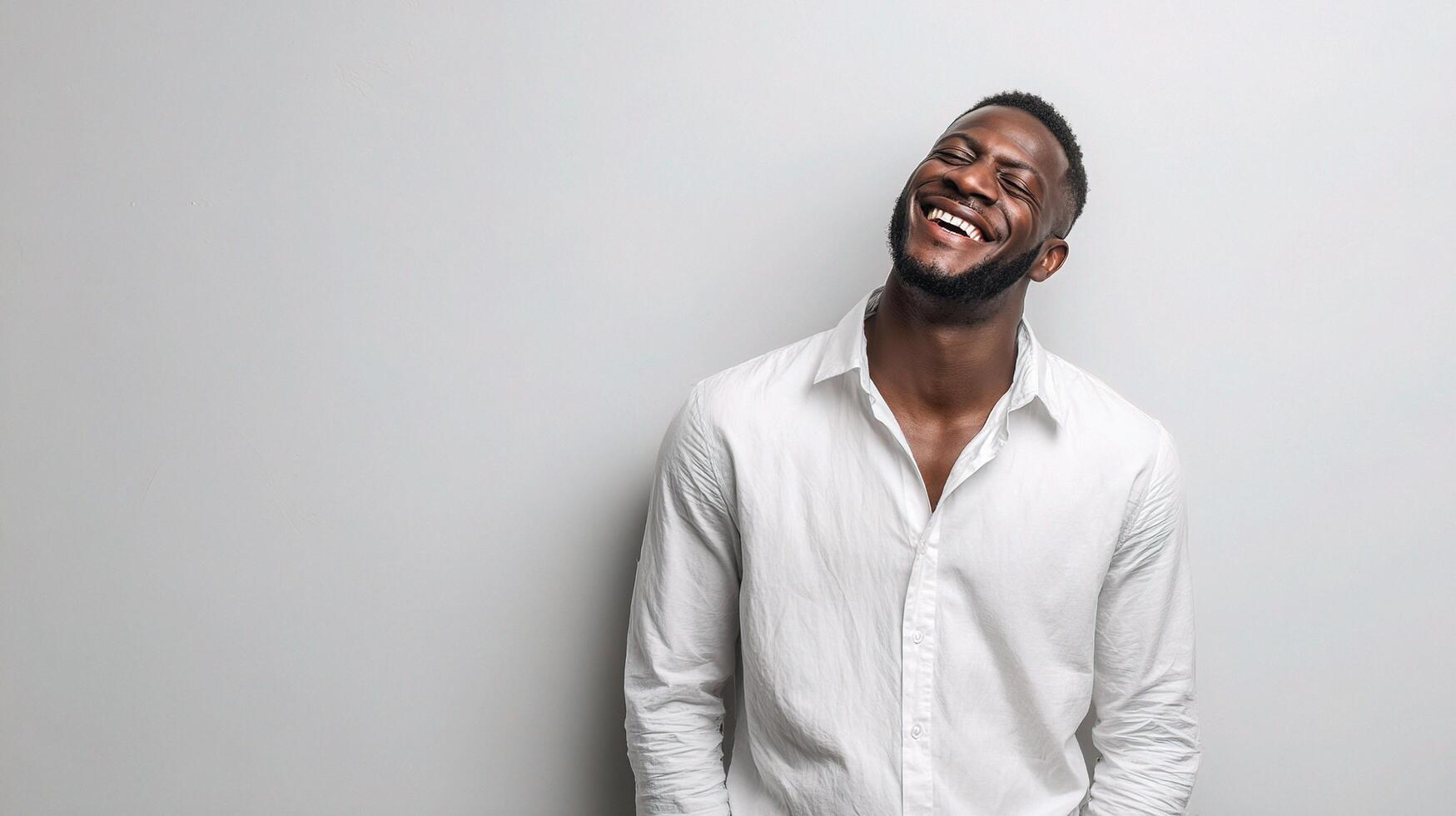 A man is laughing while standing in front of a white wall photo
