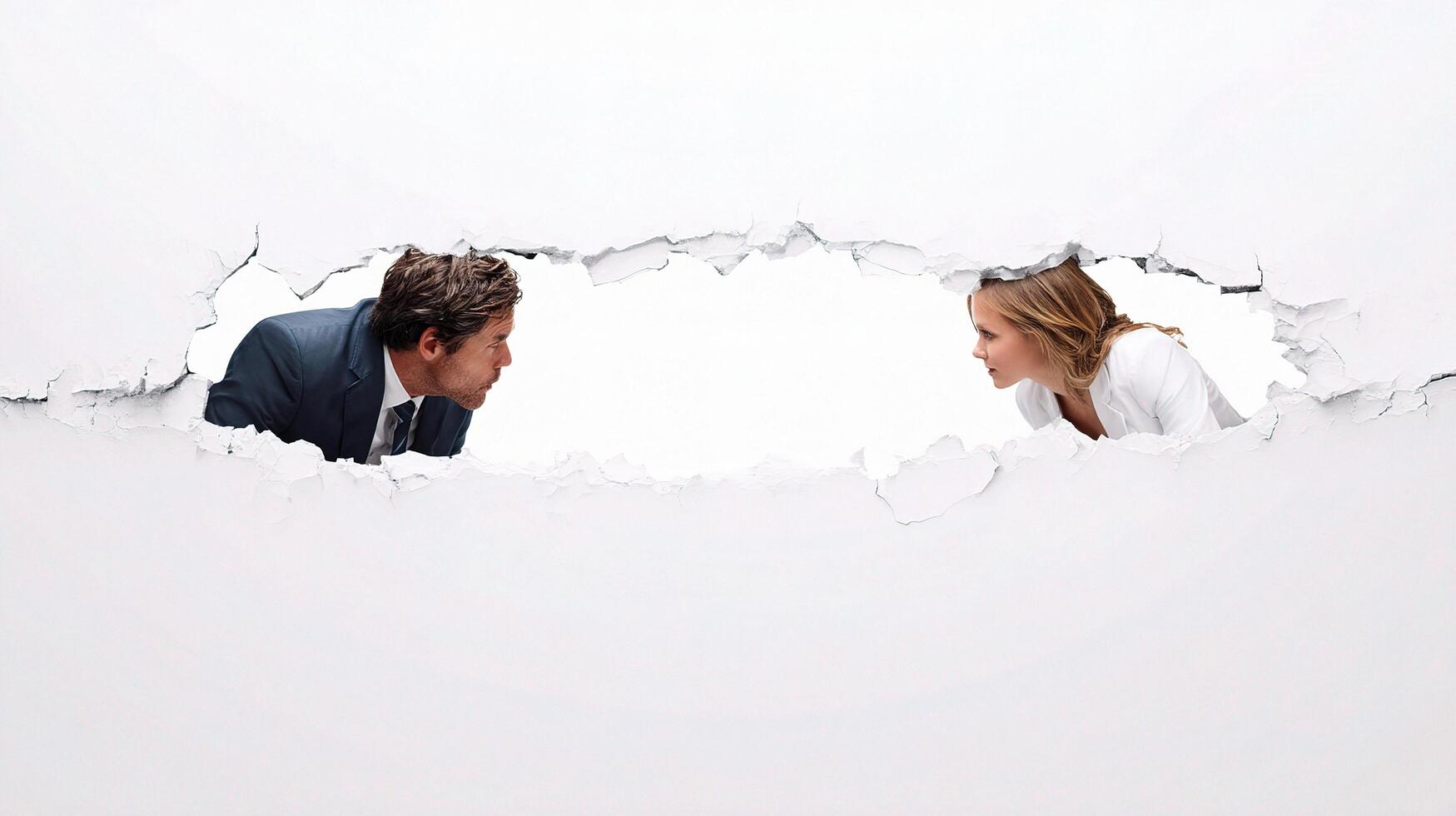 A man and woman looking at each other through a hole in a wall photo