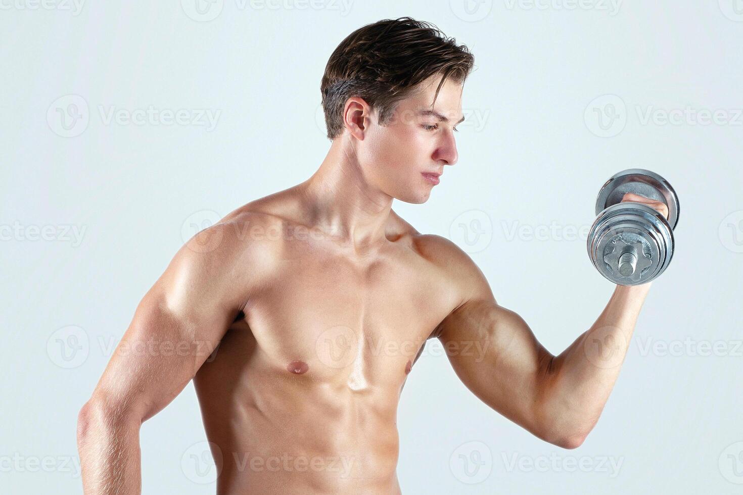 Bodybuilding strength workout. Young muscular man exercising with dumbbells, pumping up muscles on light studio background. Handsome shirtless sportsman working out with weights photo