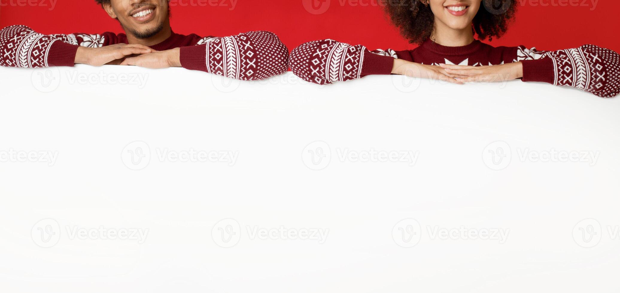 Christmas, xmas, people, advertisement, sale concept. Millennial african american male and female in sweaters lean their hands on empty white board isolated on red background, panorama, studio shot photo