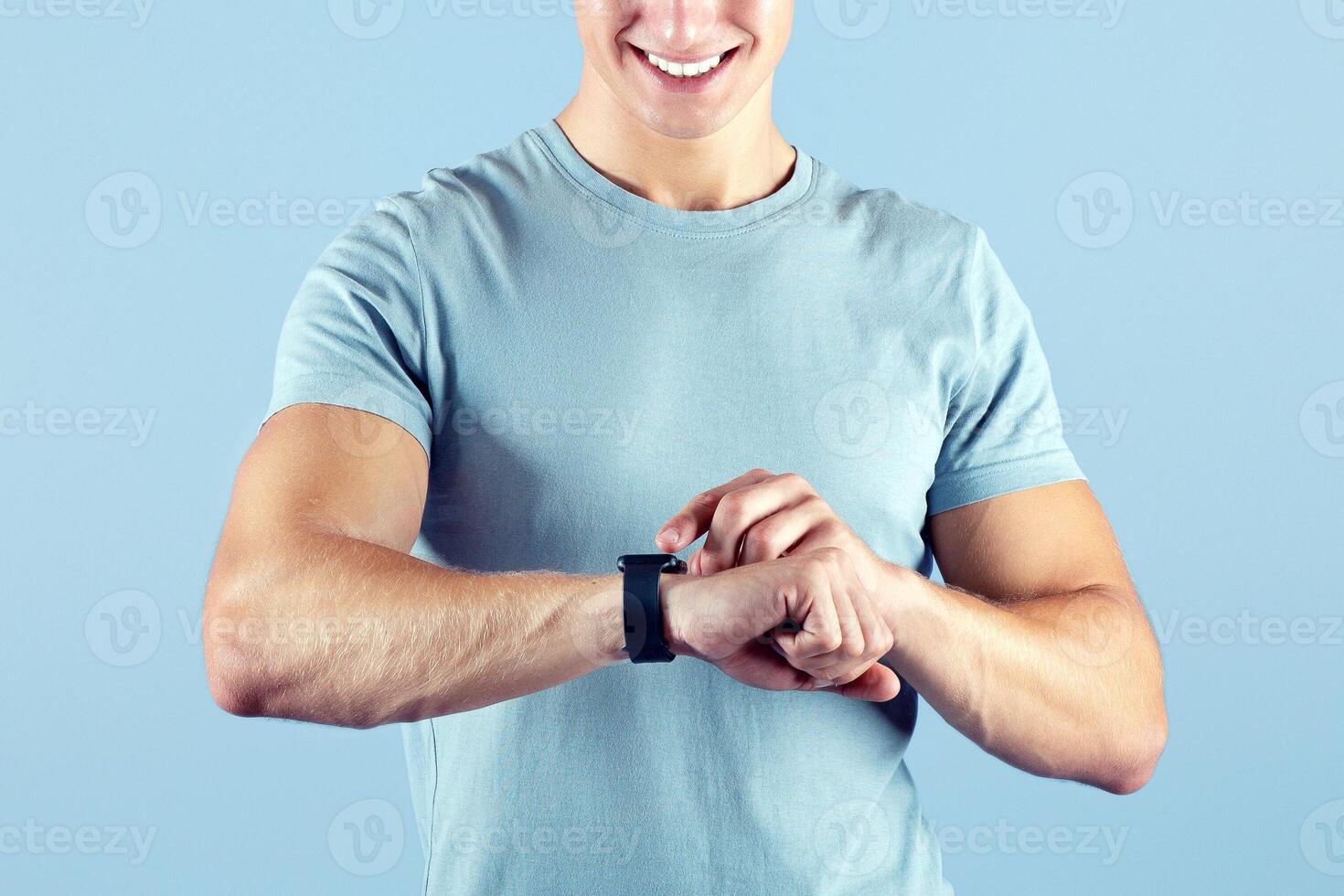 Portrait of young sporty guy checking his smartwatch on lilac studio background. Happy millennial athlete using fitness tracker during workout. Modern technologies and active lifestyle concept photo