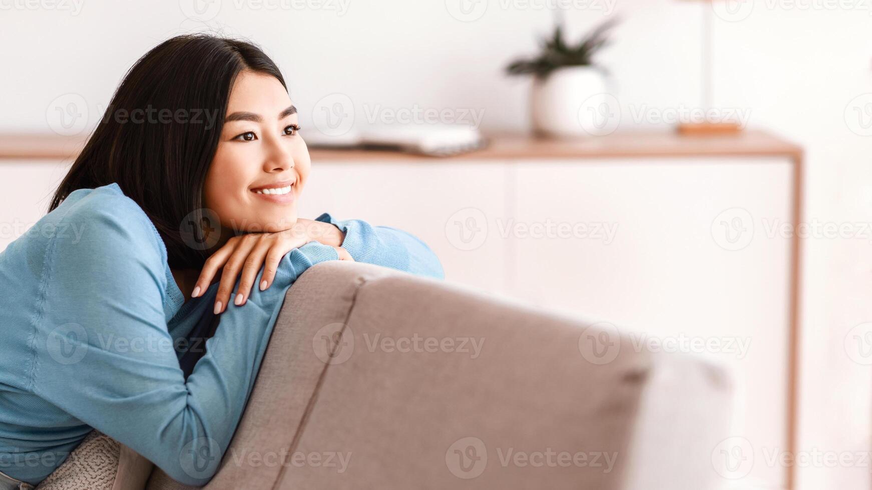 Weekend And Leisure Concept. Portrait of smiling asian woman having rest at home sitting on couch. Happy confident lady relaxing and leaning on sofa, enjoying free time and thinking about vacation photo