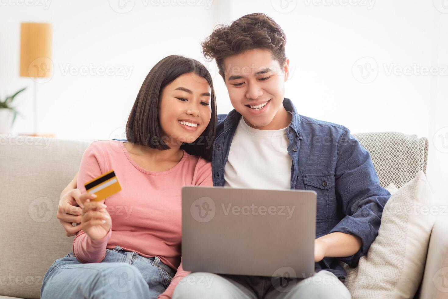 Japanese Couple Shopping Online Using Laptop And Credit Card Paying For Order Sitting On Couch At Home. Family Buying And Purchasing Things On Internet. Weekend Shopping Concept photo