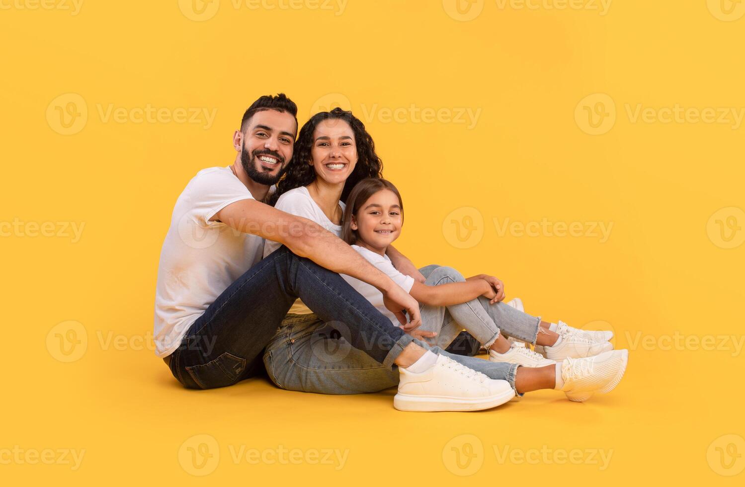 Modern Middle Eastern Family. Happy Arabic Father, Mother And Daughter Hugging Posing Together Sitting In Studio Over Yellow Background. Parents And Their Kid Smiling To Camera photo