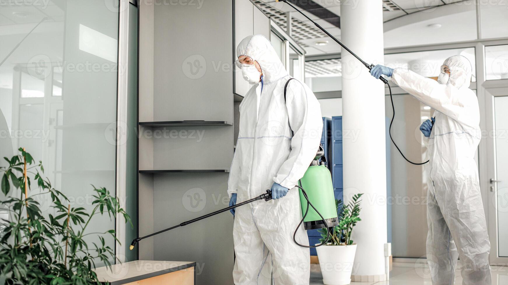 Fight against virus and protection of workers health. People in protective suits, masks and goggles with sprayer disinfectant room with chemicals during covid-19 pandemic, empty space photo