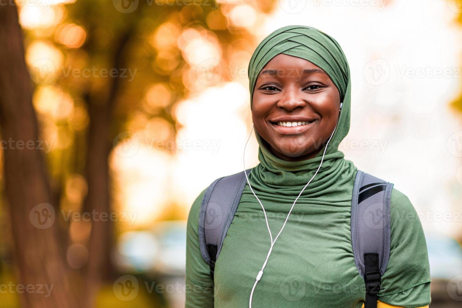 Joyful african islamic woman in headscarf listening music outdoors with smartphone and earphones, black muslim female student in hijab enjoying favorite playlist while walking in city, free space photo