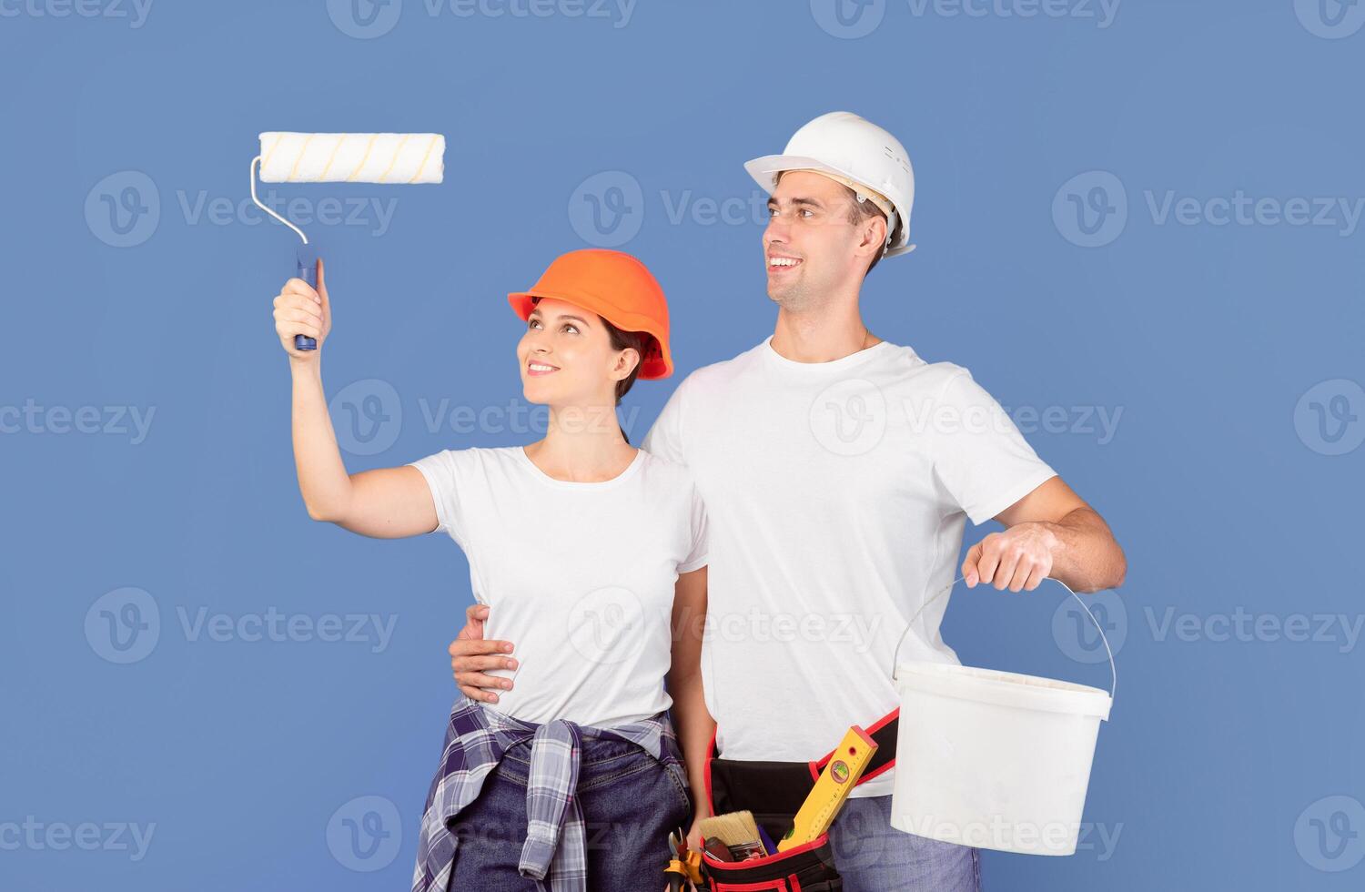 House Renovation Services. Happy Young Couple In Hardhats Holding Paint Roller And Bucket, Standing Over Blue Background, Positive Man And Woman Ready For Painting Walls And Repair, Free Space photo