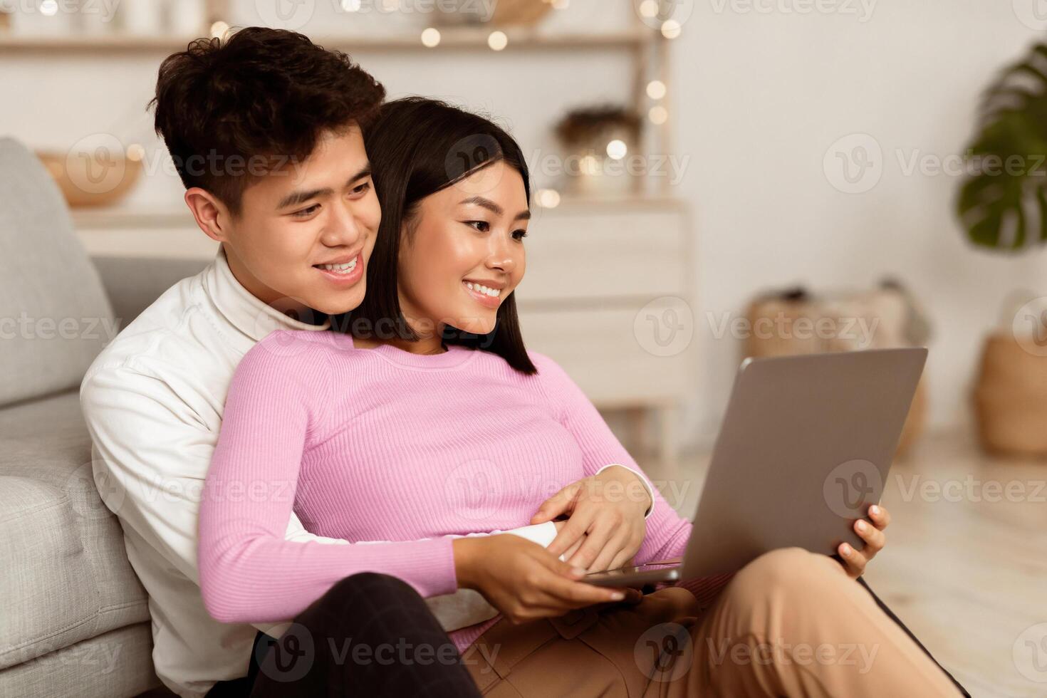 Happy Korean Couple Using Laptop Watching Movie Online Enjoying Weekend, Relaxing Sitting On Floor At Home. Evening Together, Stay-At-Home Date Leisure Concept photo