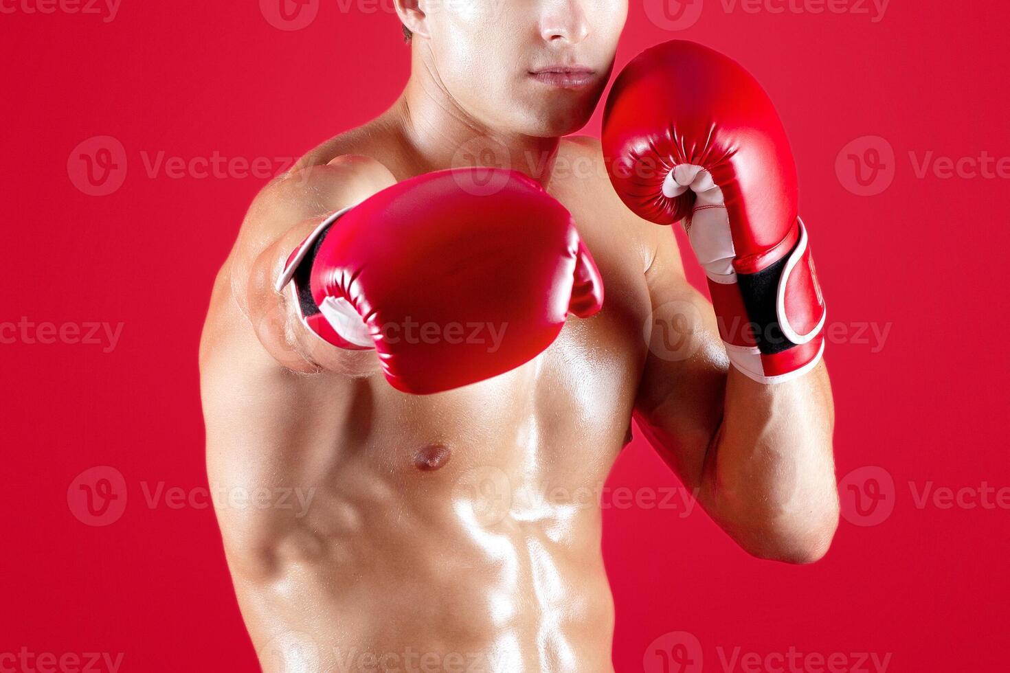 Portrait of young Caucasian man in fighting gloves practicing boxing on red studio background. Strong male boxer throwing knockout punch during his workout. Sportsman on kickboxing training photo