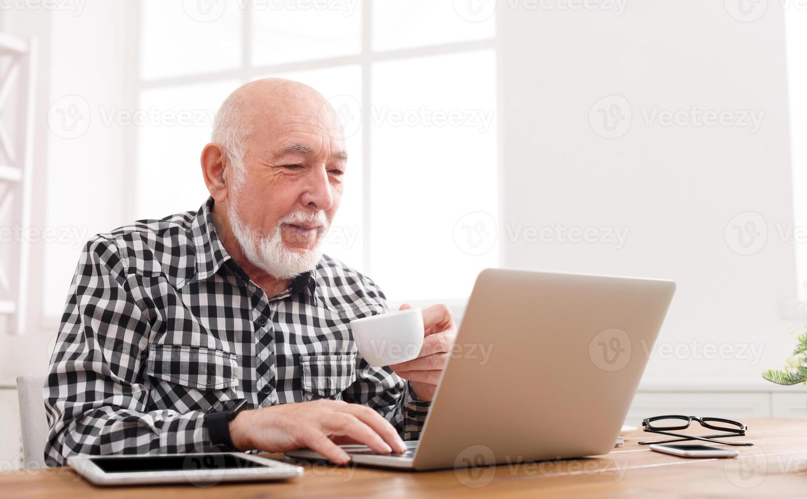 Mature man using laptop and writing in notepad at home desk. Education, recipe concept, copy space photo