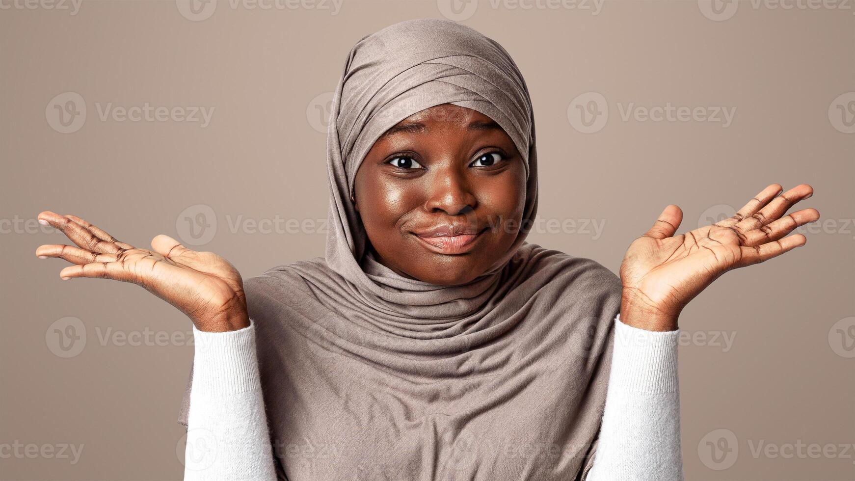 I Don't Know. Doubtful Black Muslim Lady In Hijab Shrugging Shoulders And Spreading Arms, Portrait Of Unsure African Religious Woman In Headscard Standing Over Light Studio Background, Copy Space photo