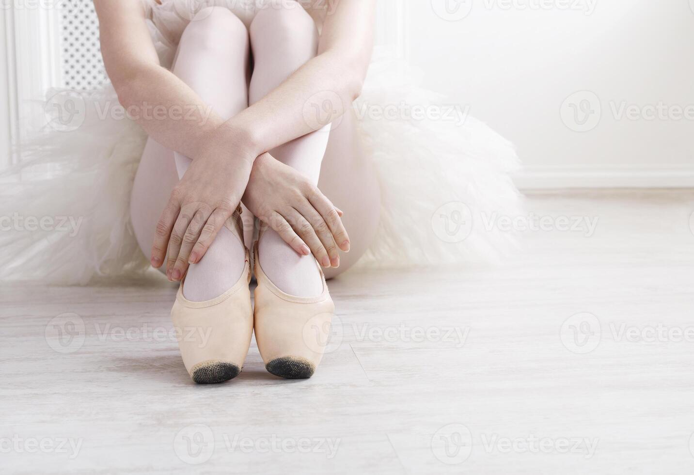 Closeup of young ballerina legs, sit in pointe shoes at white wooden floor background, with copy space. Ballet practice. Beautiful slim graceful feet of ballet dancer. photo