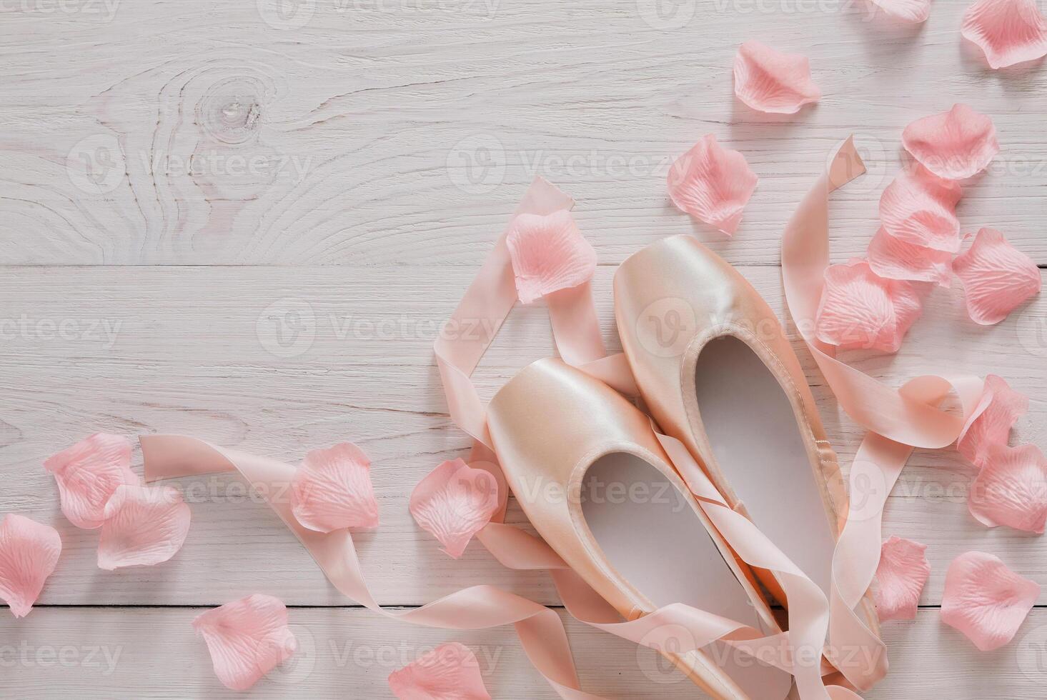 Pastel pink ballet shoes background. New pointe shoes with satin ribbon and rose petals lay on white rustic shubby chic wood, top view with copy space, soft toning photo