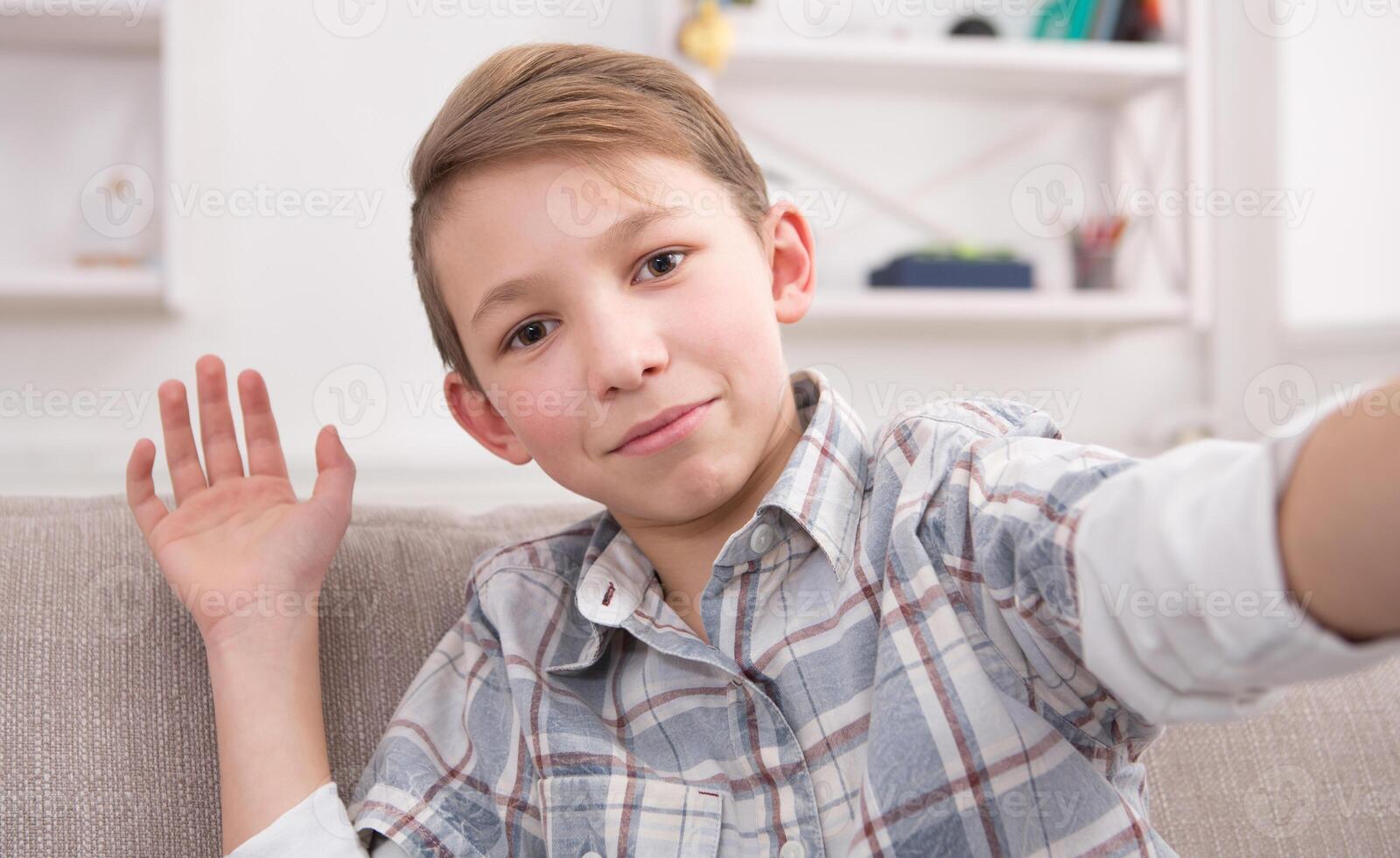 Happy child making selfie for social networks. Boy at home on sofa in living room photo