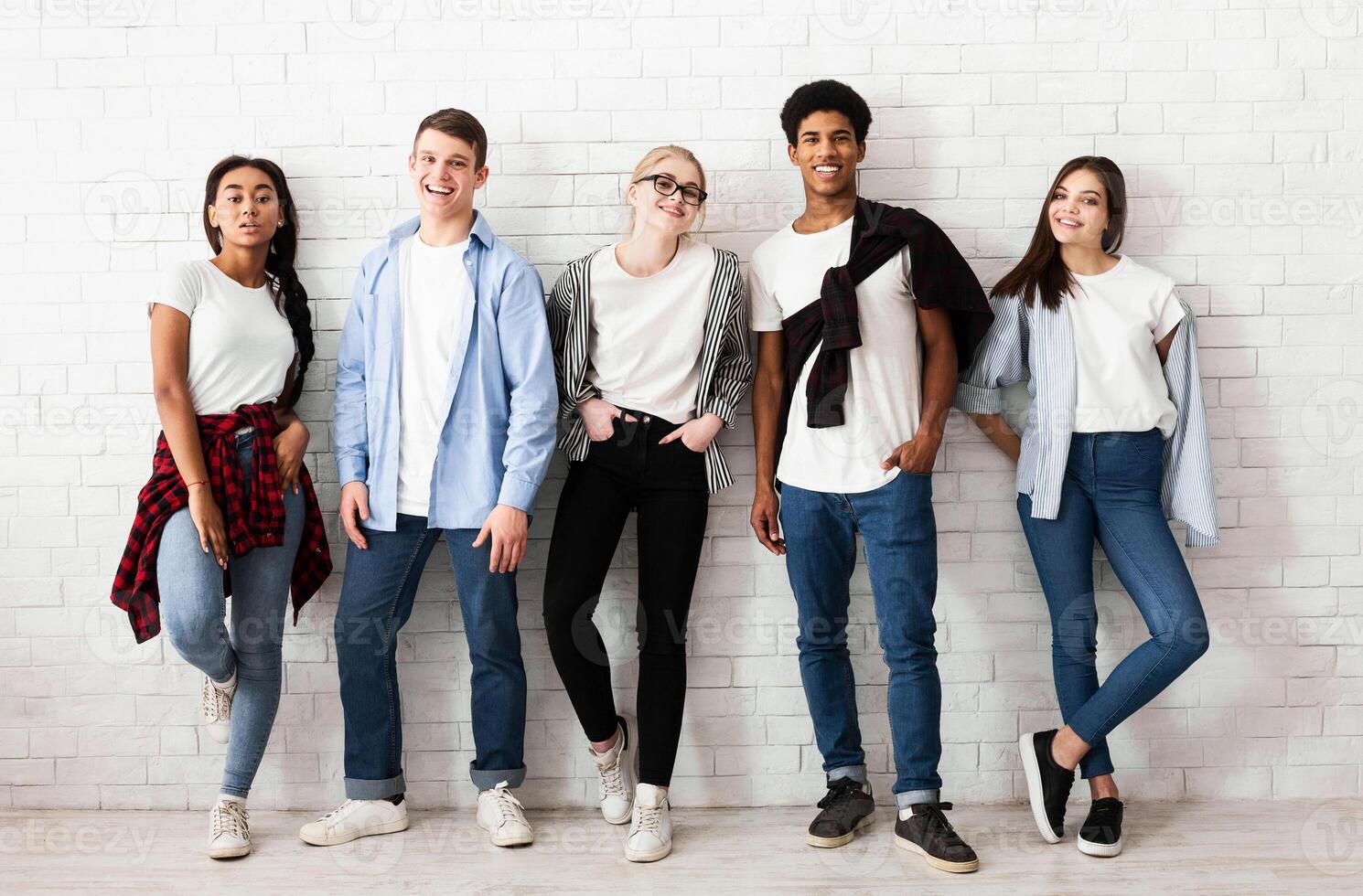 Group of stylish friends students looking at camera and posing over white wall photo