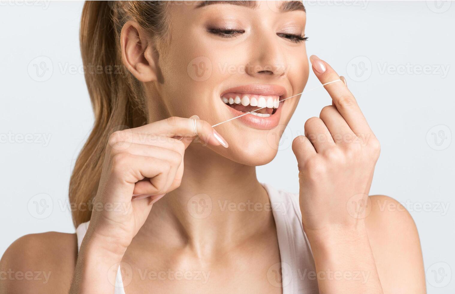 Toothcare routine. Happy young lady flossing teeth over gray background in studio. Cropped photo