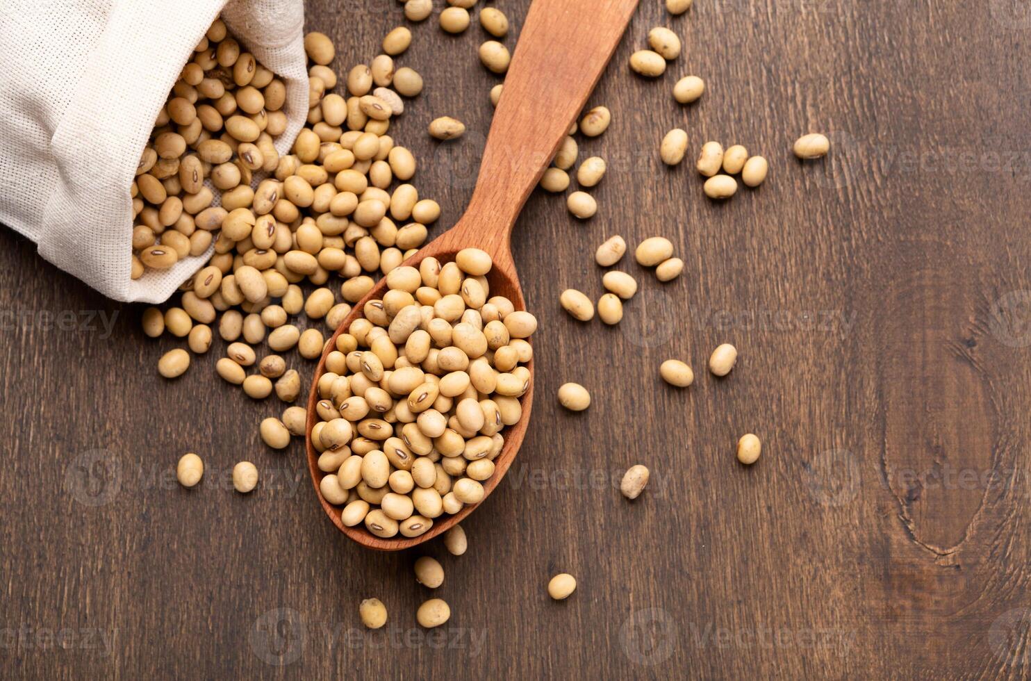 Soybeans scattered on rustic table with wooden spoon from paper bag, top view, free space photo