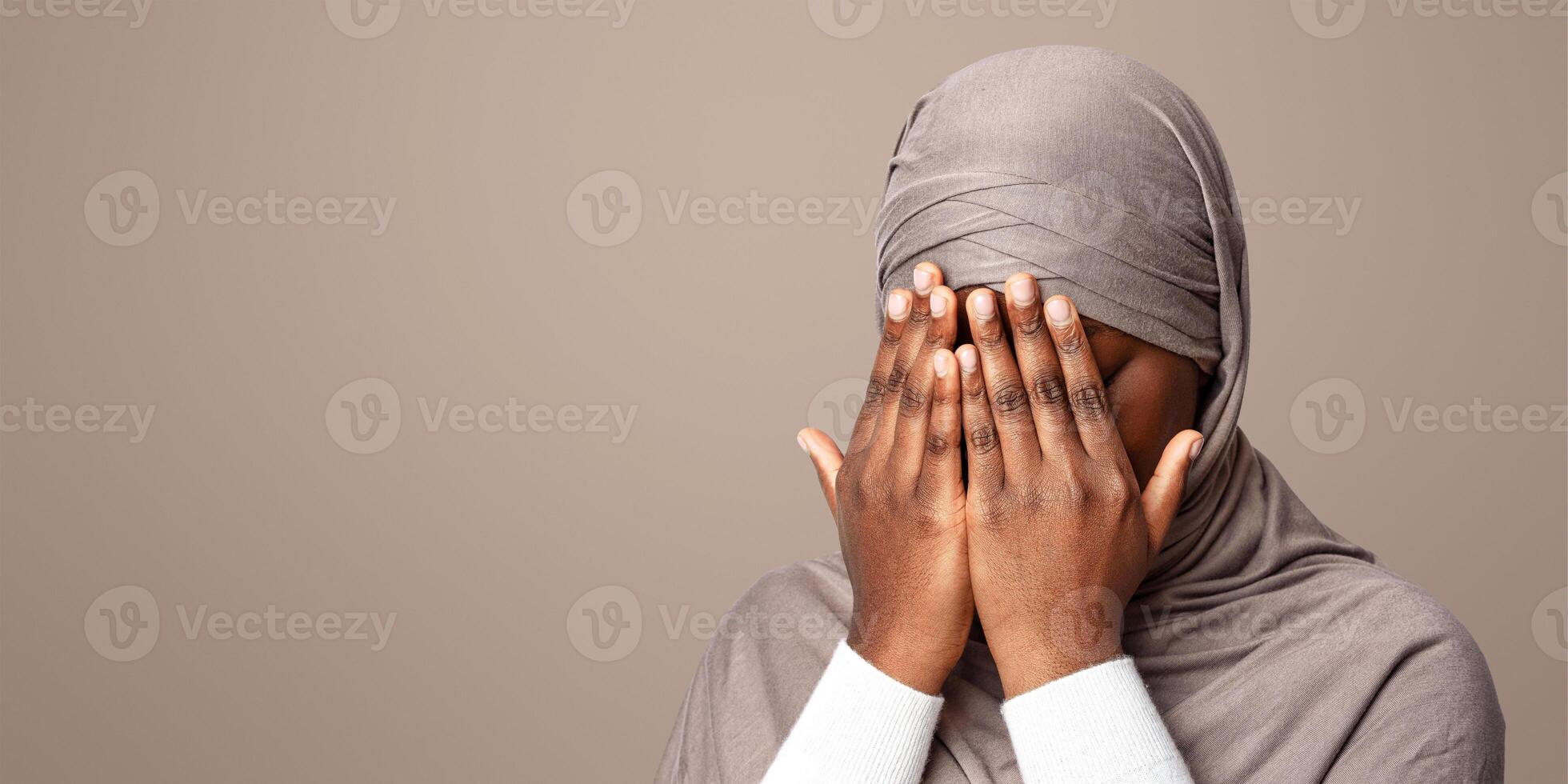 Closeup Shot Of Black Muslim Woman In Hijab Covering Face With Hands, Crying African Islamic Lady Suffering Religious Discrimination, Rasicm Or Islamophobia, Standing Over Light Background, Copy Space photo