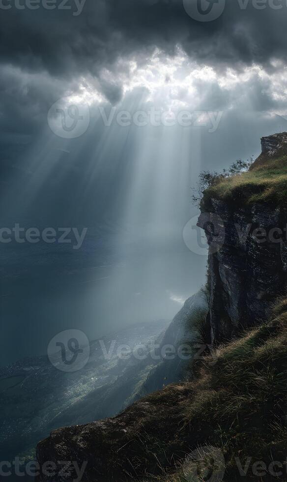 Dramatic sunbeams illuminate a rugged cliffside landscape with moody clouds and distant mountains photo