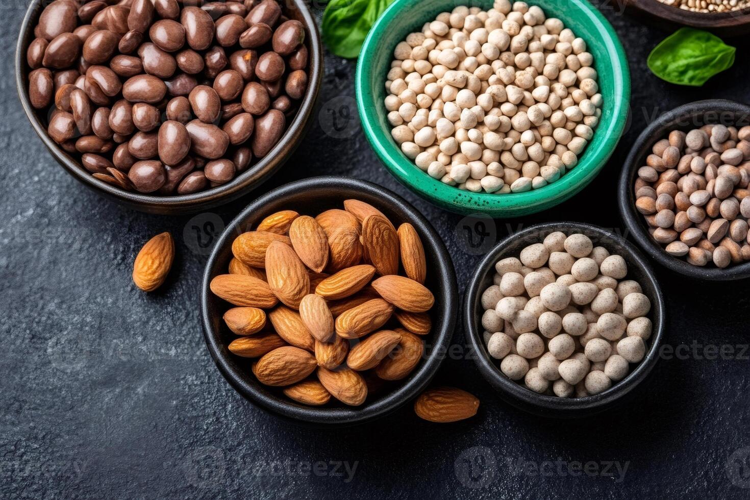 Bowls of almonds, chocolate covered peanuts, quinoa seeds, and other healthy snacks resting on dark background photo