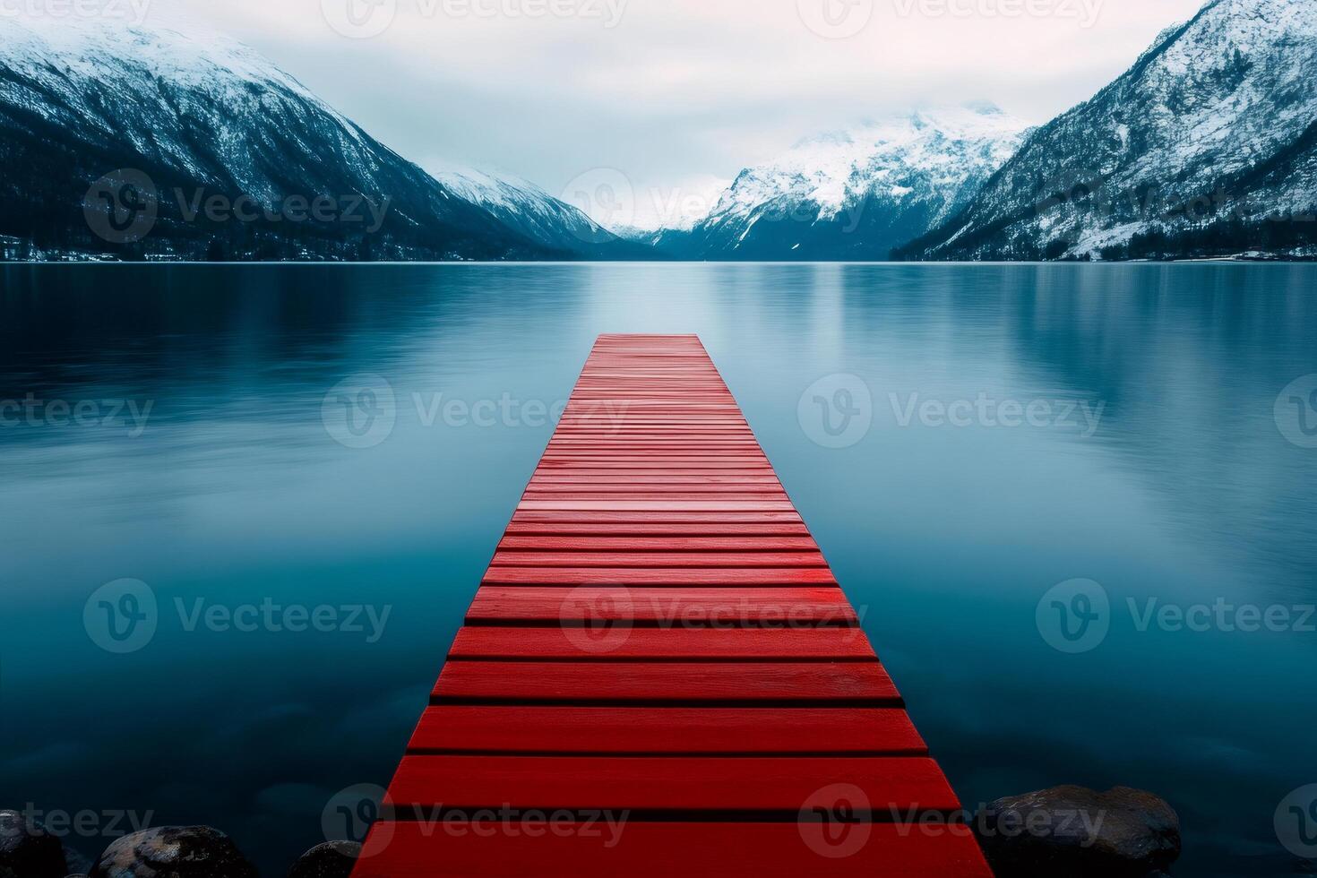Red wooden pier stretching into tranquil lake surrounded by snowy mountains photo