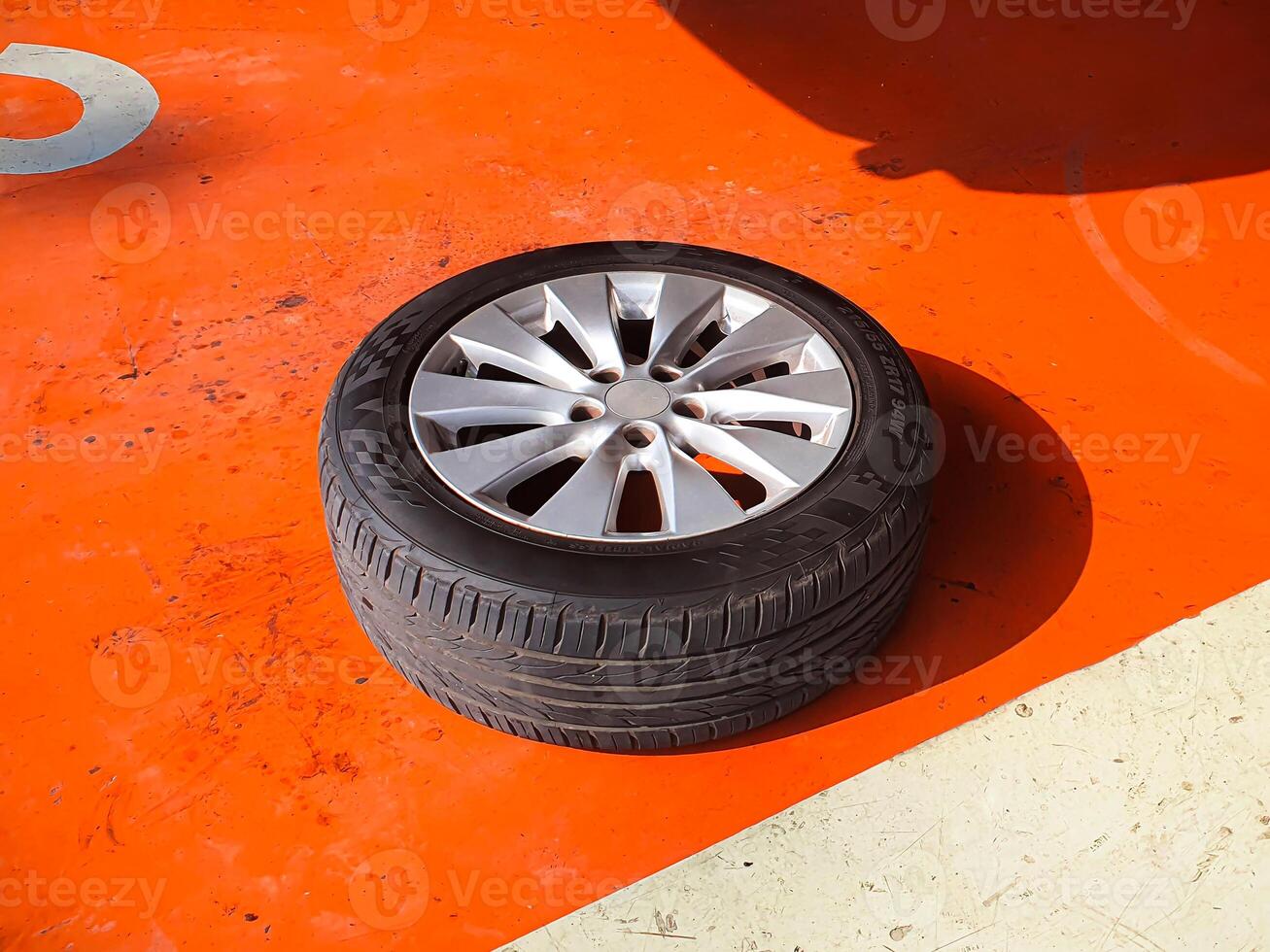 Car Wheel with Tire, A car tire mounted on a silver alloy wheel rim sits on a bright orange surface of auto repair garage. Car maintenance photo