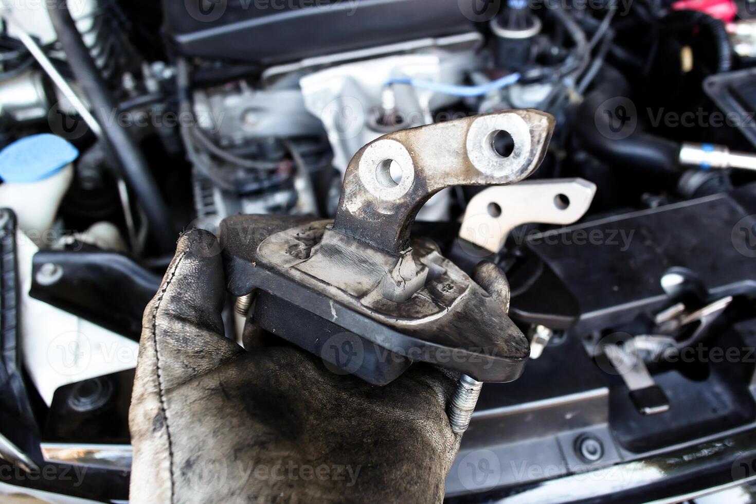 Engine Mount Replacement, Close-up of a mechanic gloved hand holding a worn out car engine mount. Car maintenance. photo