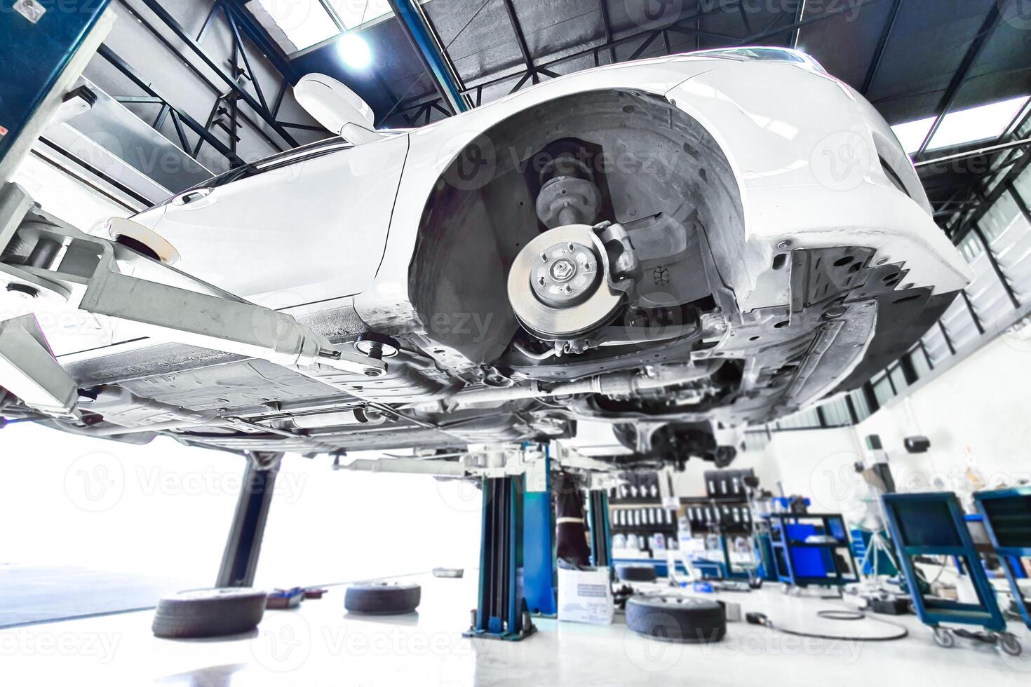 Car Repair, Auto service. White vehicle elevated on a lift in a auto repair garage with removed wheels, showing the brake system and undercarriage. photo