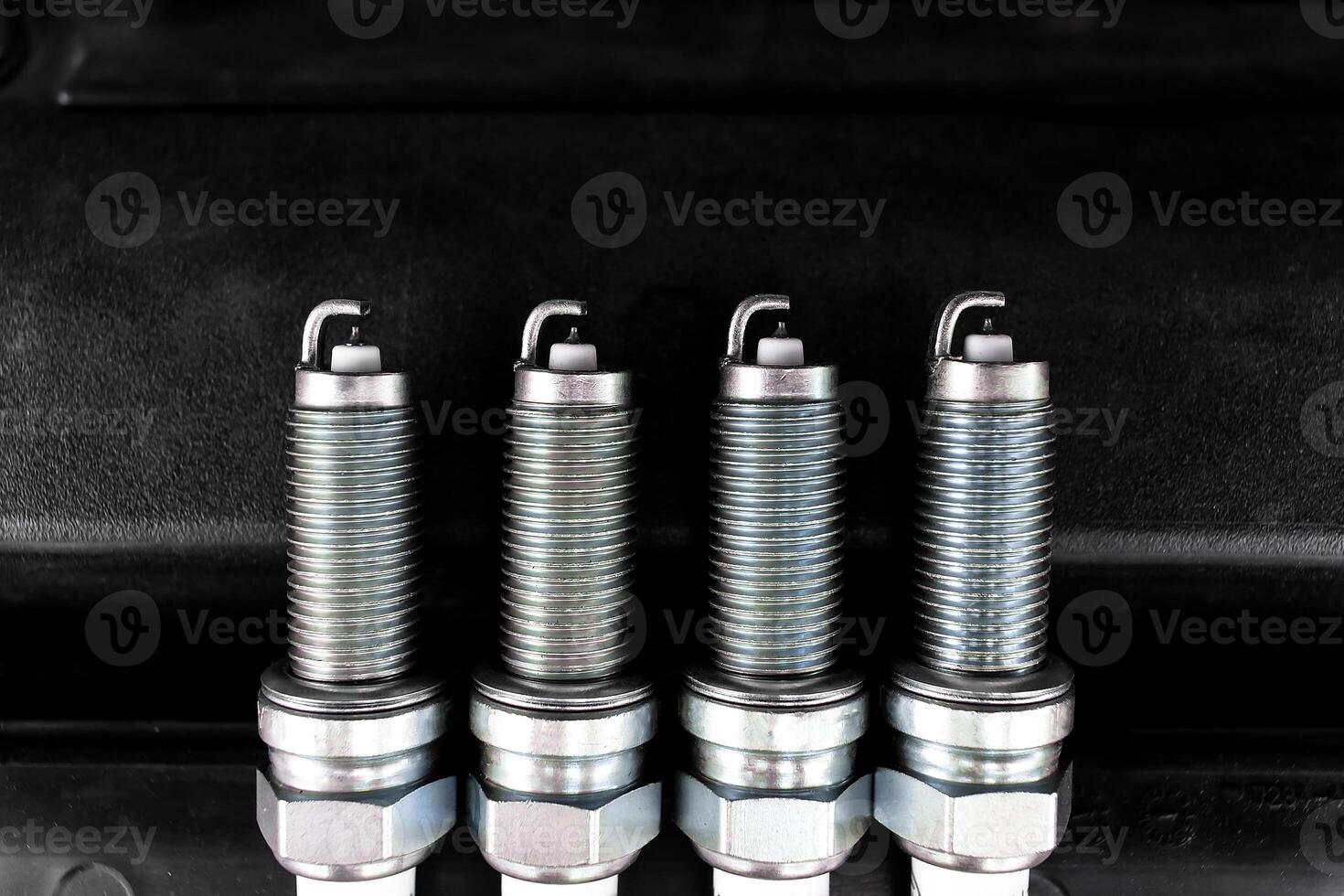 Car Spark Plugs, Close-up of four new iridium spark plugs are lined up against a dark background. DIY engine repair photo