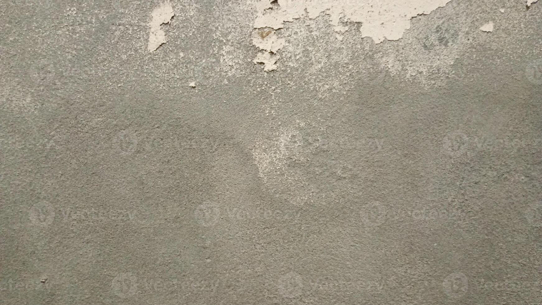 A closeup of a rough, worn-out concrete wall with a gritty texture, featuring cracks and crevices. The color is a dull, muted gray with subtle variations in shade, showing off the uneven surface. photo