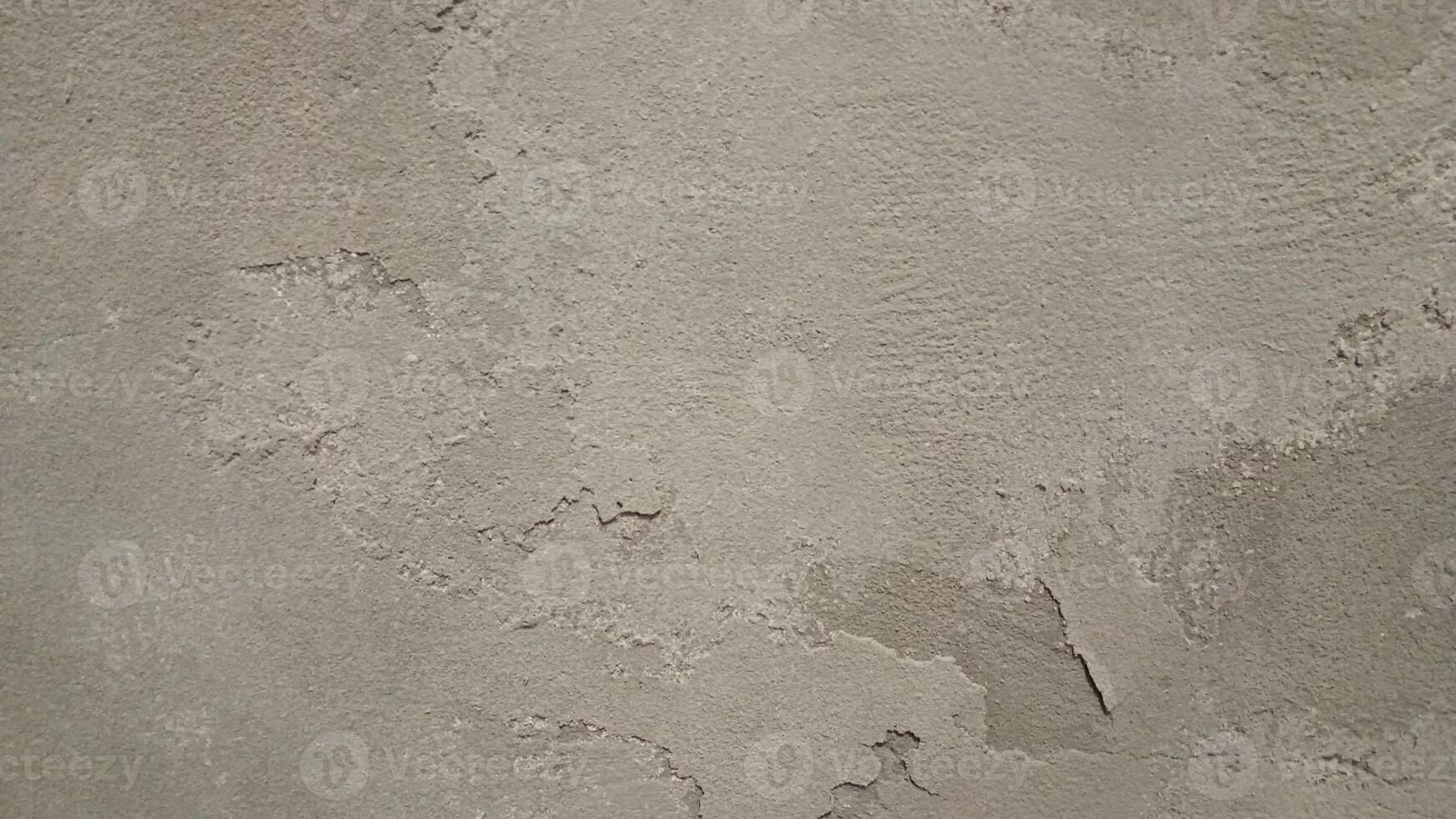 Close-up of a rough, worn-out concrete wall with a gritty texture, featuring cracks and crevices. The color is a dull, muted gray with subtle variations in shade, showing off the uneven surface. photo