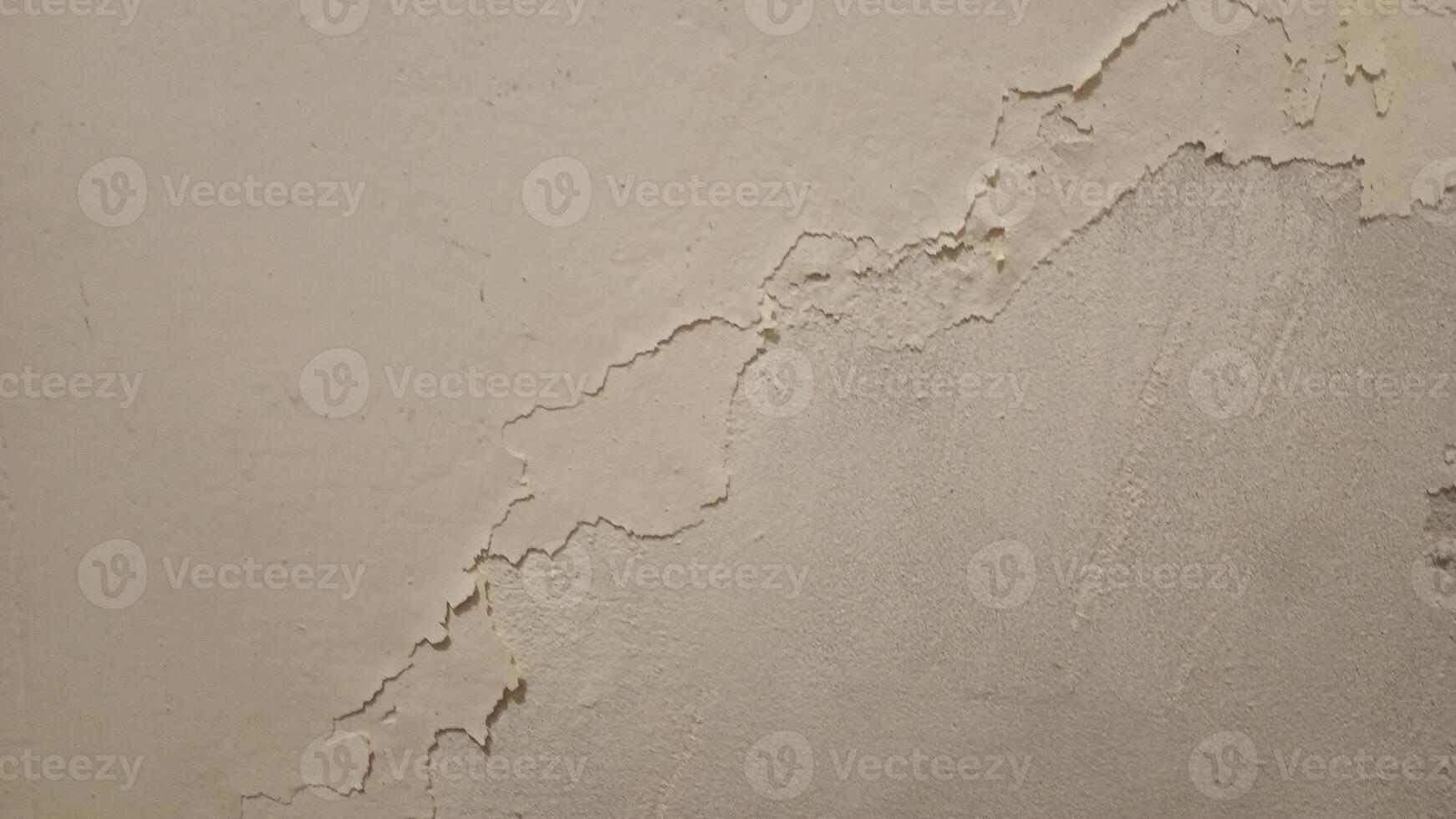 A close up of a rough, worn-out concrete wall with a gritty texture, featuring cracks and crevices. The color is a dull, muted gray with subtle variations in shade, showing off the uneven surface. photo