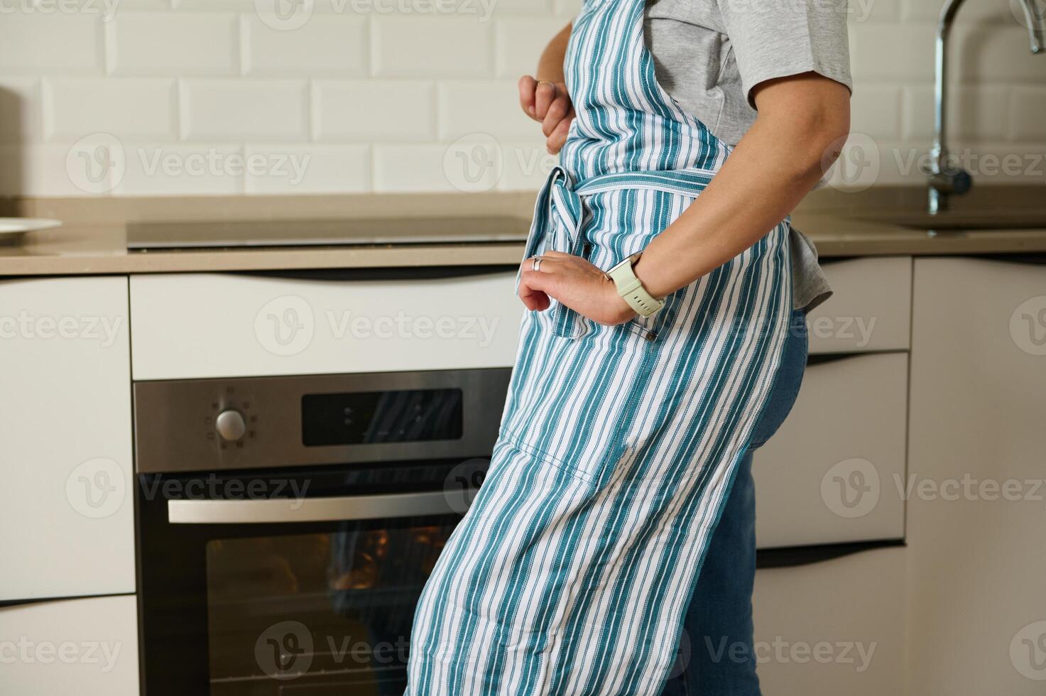 Person Wearing Apron Standing in Modern Kitchen Near Oven photo