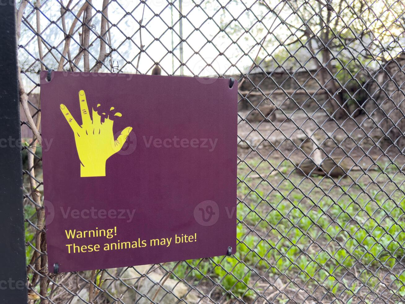 Warning sign on zoo enclosure fence showing bitten hand and message. These animals may bite to caution visitors and promote safety awareness around wild animals photo