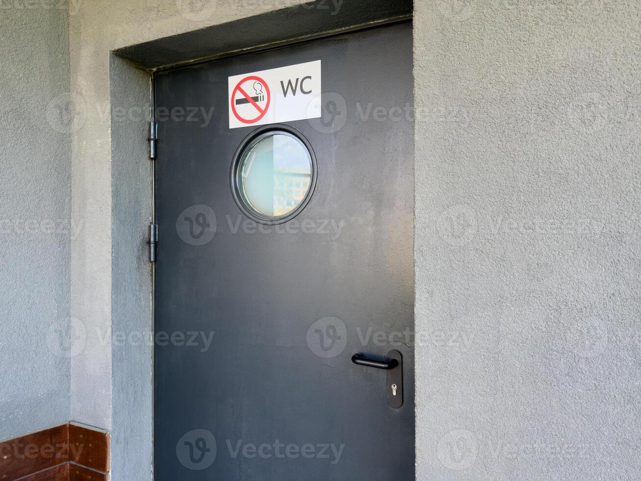 Black door with round frosted window and no smoking WC sign mounted on rough gray wall, marking entrance to public restroom with emphasis on clarity, hygiene and behavioral regulation in urban setting photo