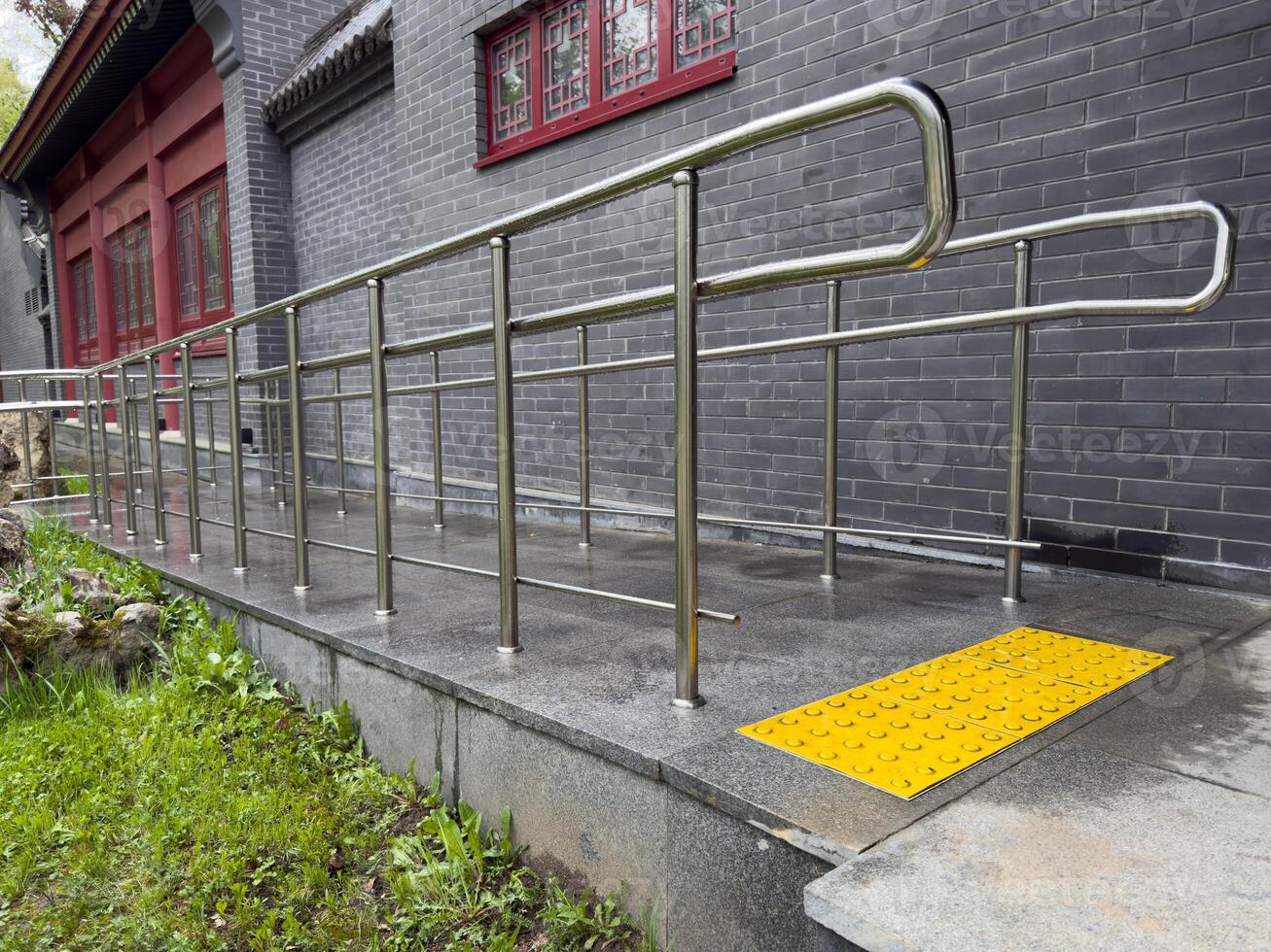 Stainless steel accessibility ramp with bright yellow tactile paving for visually impaired individuals, located next to building, highlighting inclusive design and care for people with disabilities photo
